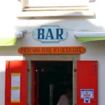 "Mieux vaut boire ici qu'en face" devise inscrite au dessus de la porte d'entrée d'un bar.